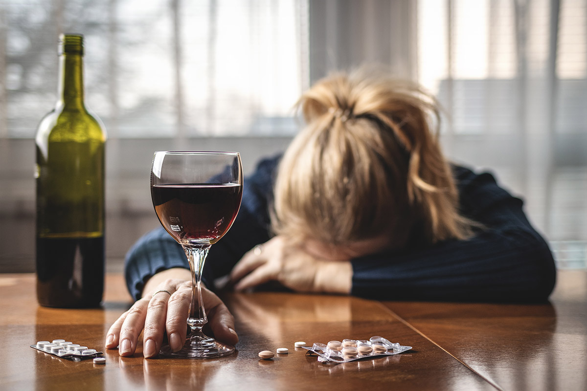 woman with head down on table and glass of wine and pills dealing with relapse in drug and alcohol addiction