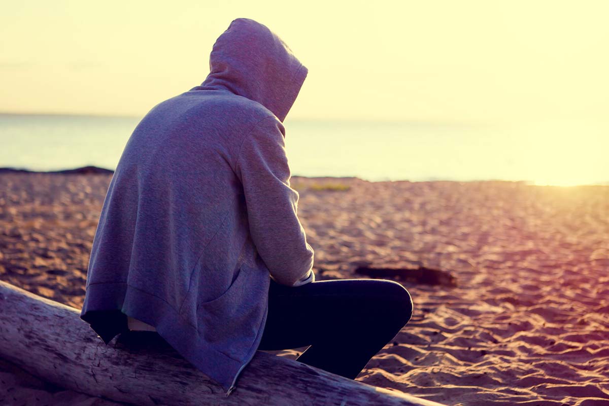 what is a speedball, person wearing a hoodie sitting on beach looking out at sunrise/sunset