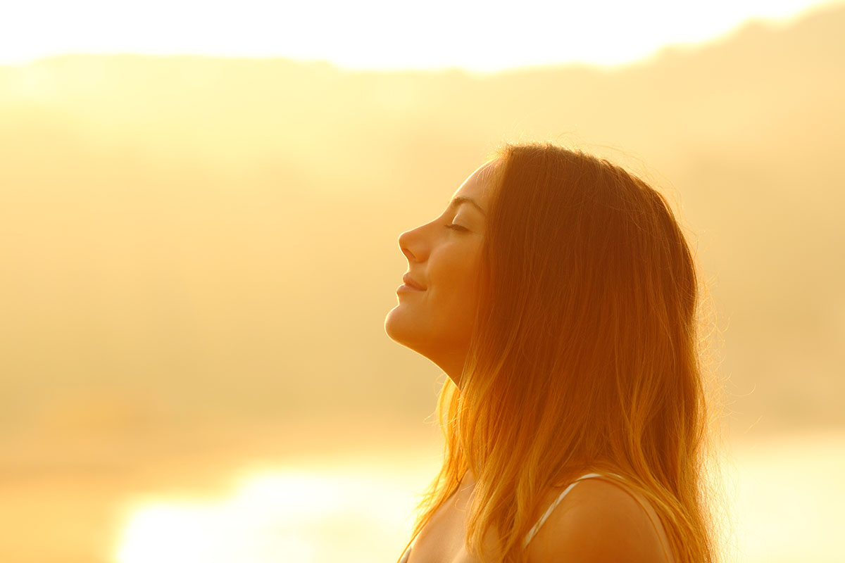 recovery from addiction, woman outside smiling as the sun shines down on her face