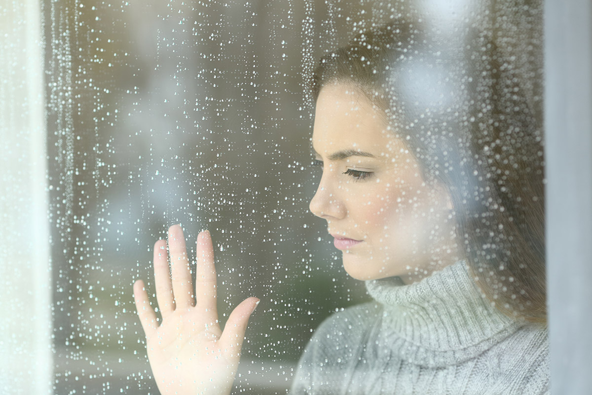 woman looking out rainy window thinking about common mental health disorders and addiction