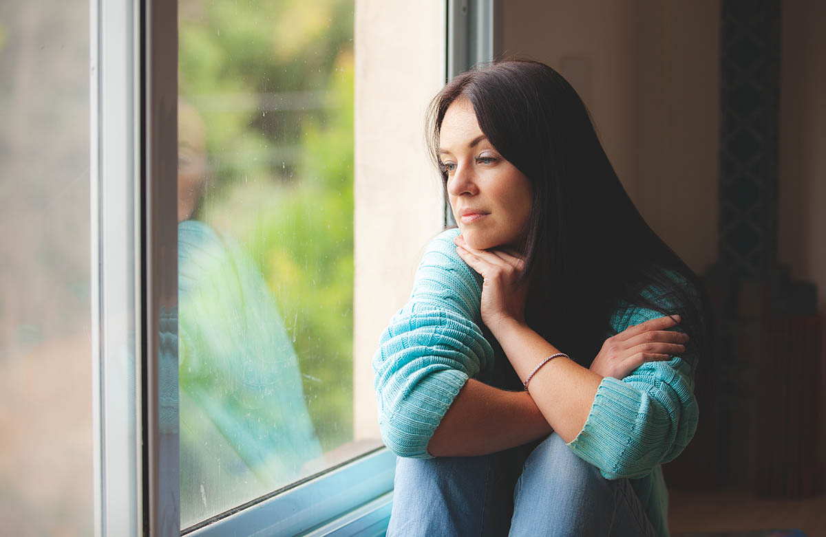 woman looking out window and struggling with quarantine and relapse